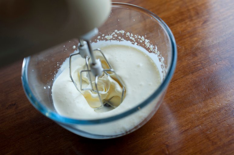 Closeup view of the metal whisk on an electric kitchen mixer while whisking double cream in a clear glass mixing bowl