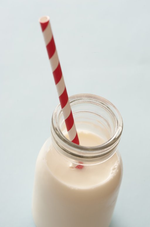Glass bottle full of milk served with a striped red and white straw over a light grey background with copy space for a healthy drink rich in calcium