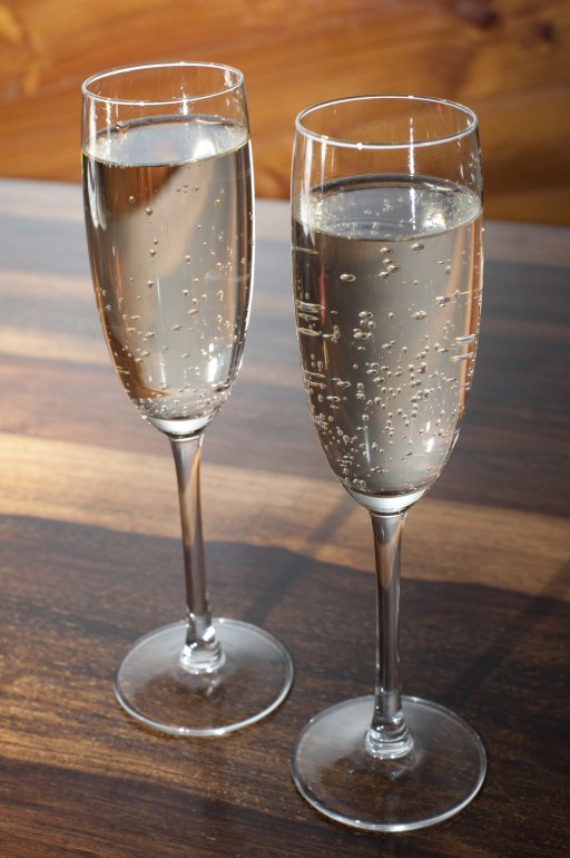 Two full flutes of champagne or sparkling white wine standing side by side on a wooden counter conceptual of a romantic evening or celebration