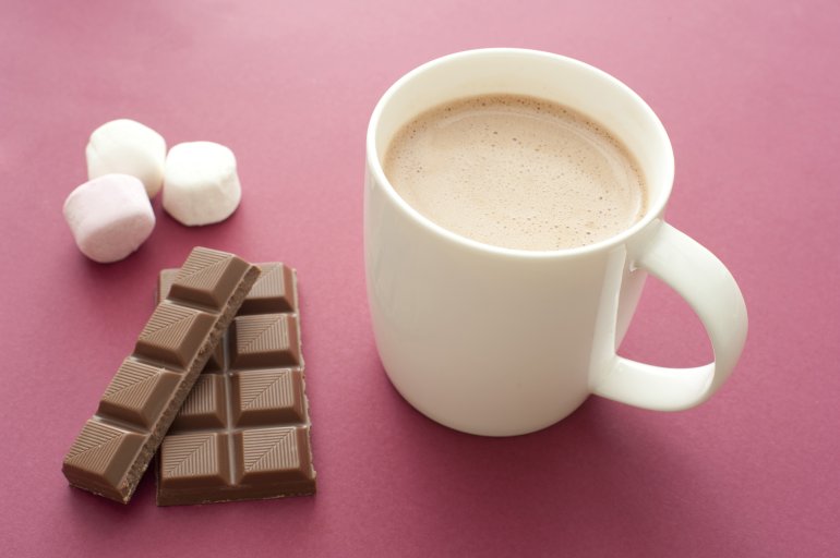 Delicious hot chocolate drink in a mug with ingredients alongside including a bar of chocolate candy and marshmallows, on a red background, high angle view