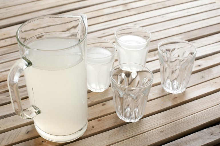 Fresh homemade lemonade in a jug sitting on wooden picnic table with two full and two empty glasses for a refreshing summer drink
