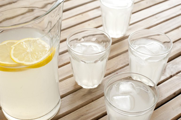 Refreshing homemade fresh lemonade with slices of lemon served on a wooden picnic table with four full glasses and a jug