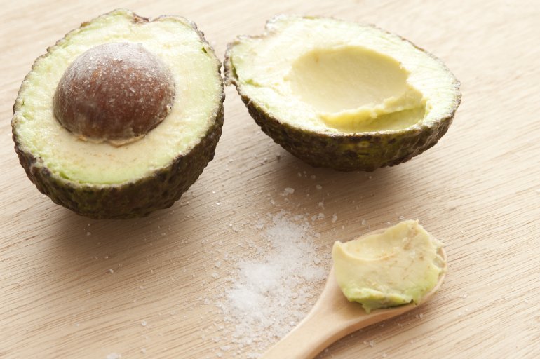 Delicious halves of avocado with salt and spoon on wooden table