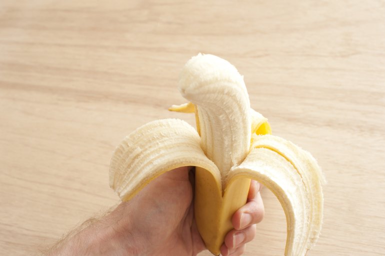 Uncorked banana in man's hand against of wooden background
