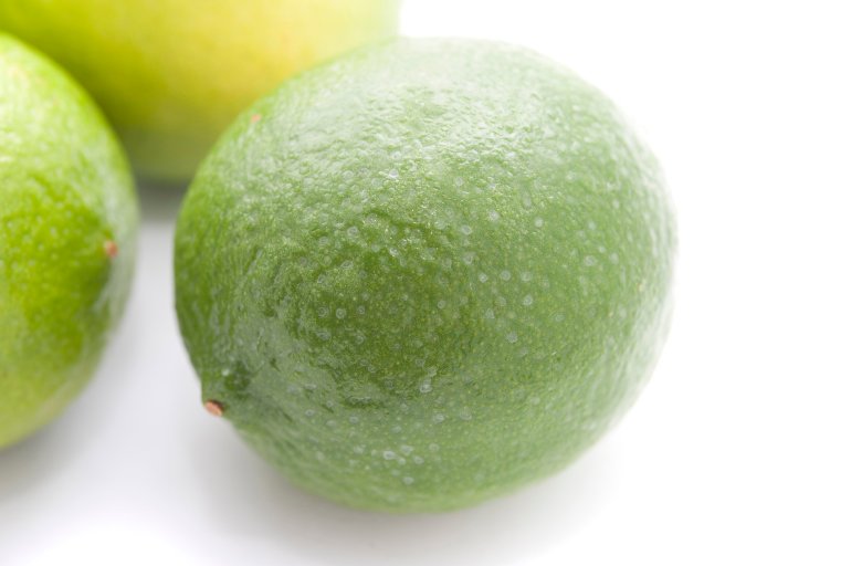 Whole fresh green limes used in cooking for their tangy acidic taste as a flavouring and garnish, on a white background