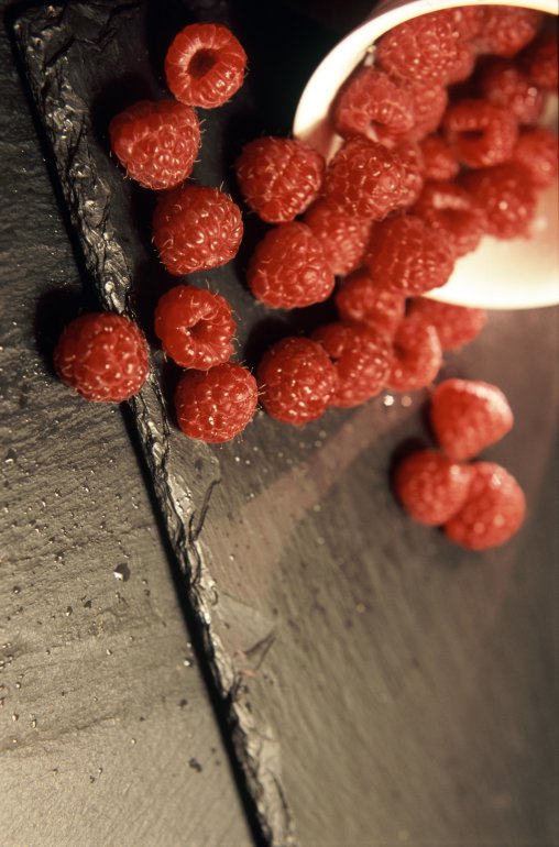 Delicious healthy ripe red raspberries spilling from a small ceramic container onto an old wooden surface with copyspace