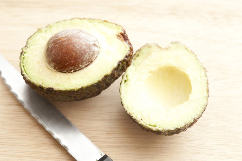 Fresh cut avocado with seed and knife on wooden table