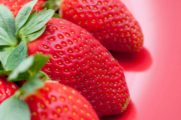 Close-up of tasty fresh strawberries with green leaves, on red background