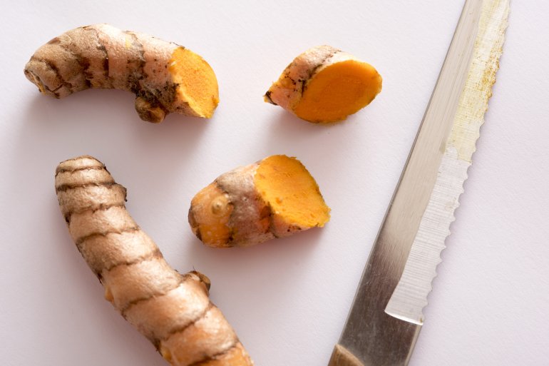 Fresh turmeric cut with a kitchen knife, viewed from above on white surface