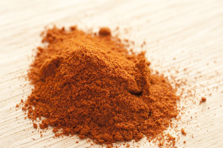 Pile of red hot paprika powder in close-up on white wooden table surface