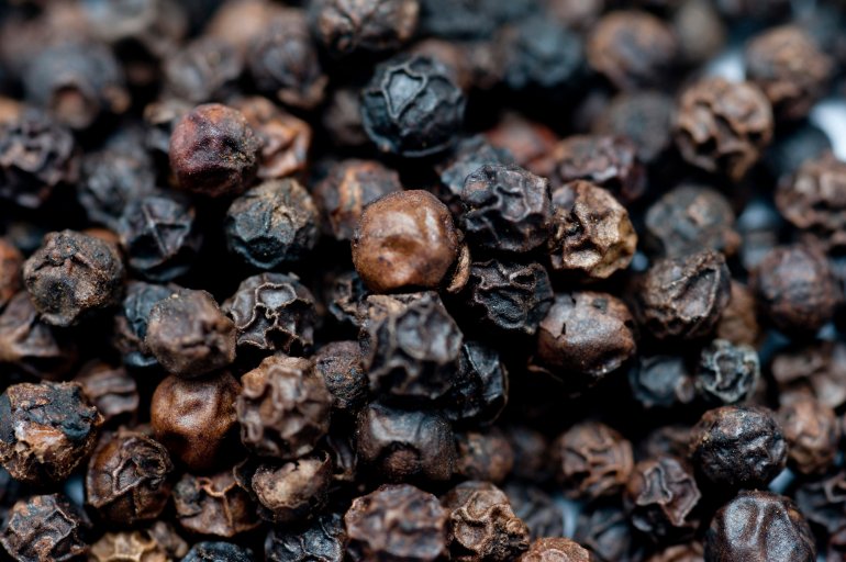 Background of dried black peppercorns which are ground and used as a spice, seasoning, and condiment in cookery