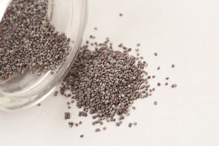 Pouring out poppy seeds from a glass bowl onto white table surface, viewed in close-up