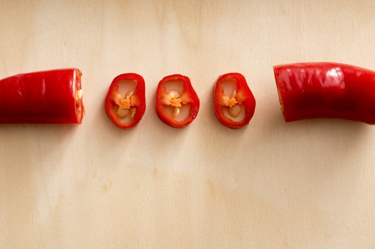 Sliced long red hot chilli pepper in close-up over beige surface with copy space