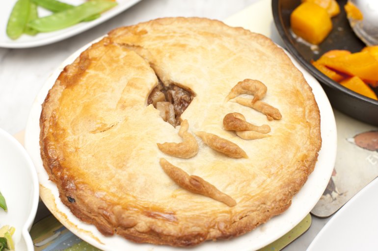 Tasty homemade meat pie with a golden pastry crust ready to be served with vegetables, close up high angle view