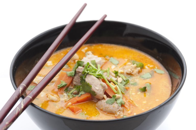 Delicious bowl of Peranakan cuisine laksa soup with meat, herbs, carrots and chopsticks on top