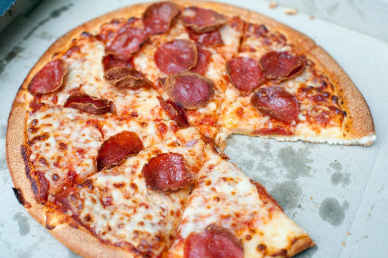 Close up view of a takeaway cheese and pepperoni or salami pizza sliced into portion with one slice removed still in the traditional disposable cardboard pizza box