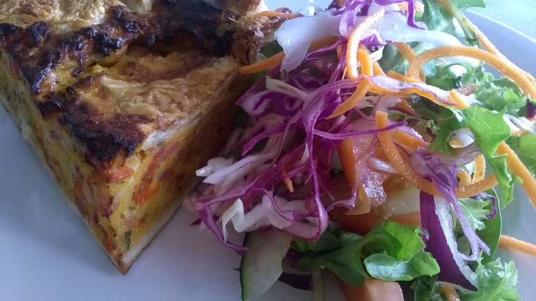 Close up on slice of baked quiche beside red cabbage, onion, lettuce and carrot salad