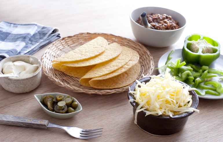 Ingredients for preparing fresh Mexican tacos spread out in individual dishes around a basket of empty tacos ready and waiting