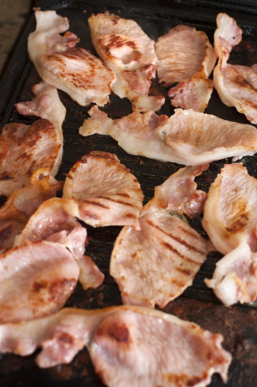 Overhead view of crispy grilled bacon rashers cooking on a griddle ready for a delicious breakfast, full frame background