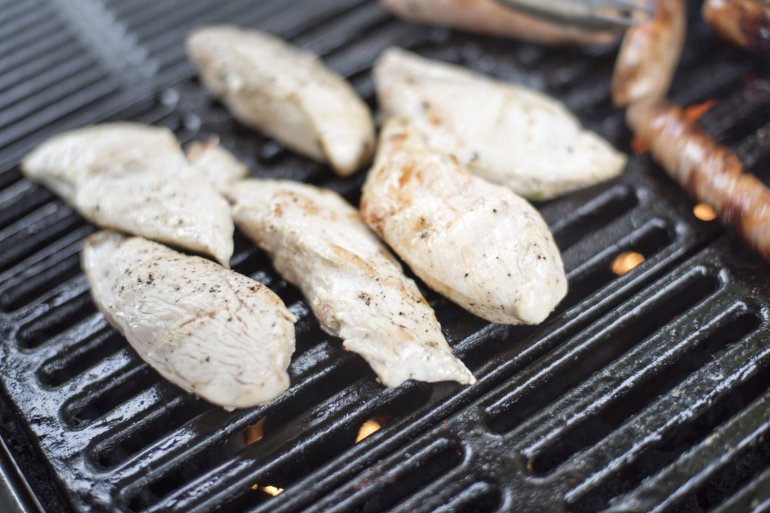 Chicken fillet pieces being prepared on thick barbecue grid, viewed in close-up from high angle