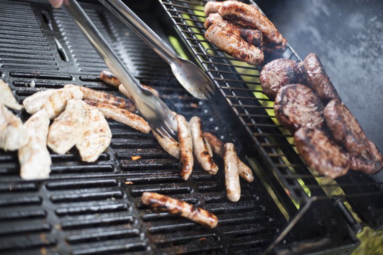 Assorted meats cooking over the coals at a BBQ with chicken breasts, sausage and burger patties