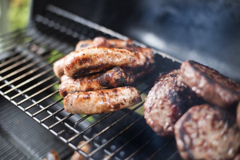 Meat grilling over a barbecue fire with a close up view on beef patties and pork sausages