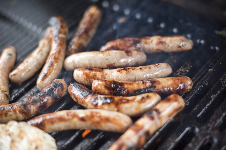 Sausages being prepared on thick barbecue grid, viewed in selective focus close-up from high angle