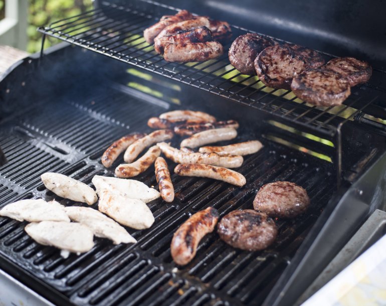 Assorted meat grilling over a BBQ fire with chicken breasts, sausages and beef patties