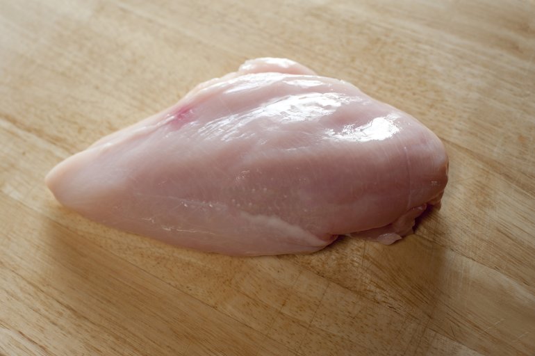 One uncooked chicken fillet on wooden board. From above