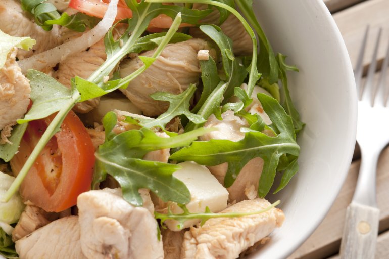 A close up of a healthy chicken salad dish with rocket on a table with fork.