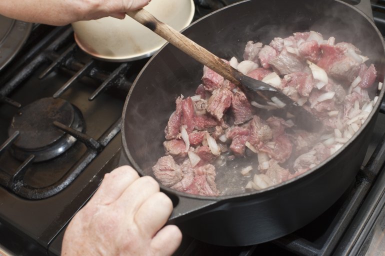 Man cooking a stew stirring the browning beef and onion mix in a frying pan over a hotplate as he browns the meat to seal in the flavour
