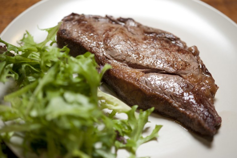 Low angle view of a juicy grilled sirloin steak plated with fresh leafy green salad on a white plate