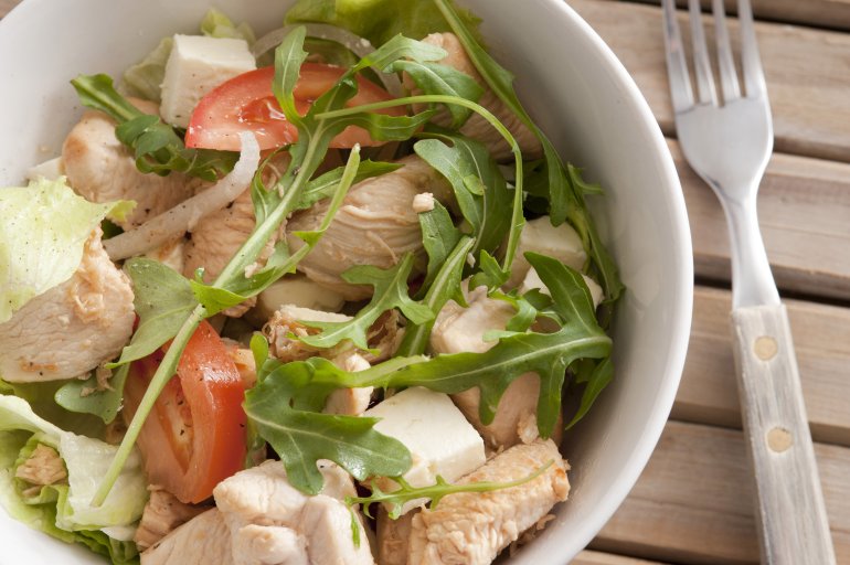 Healthy salad with chicken pieces and fresh green rocket, tomato and onion served in a bowl with a fork viewed top down