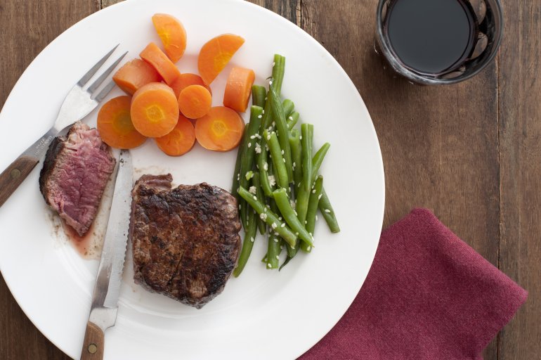 Steak meal with fresh steamed vegetables, carrots and fresh green string or runner beans, viewed high angle with the steak cut through to show the tender juicy meat
