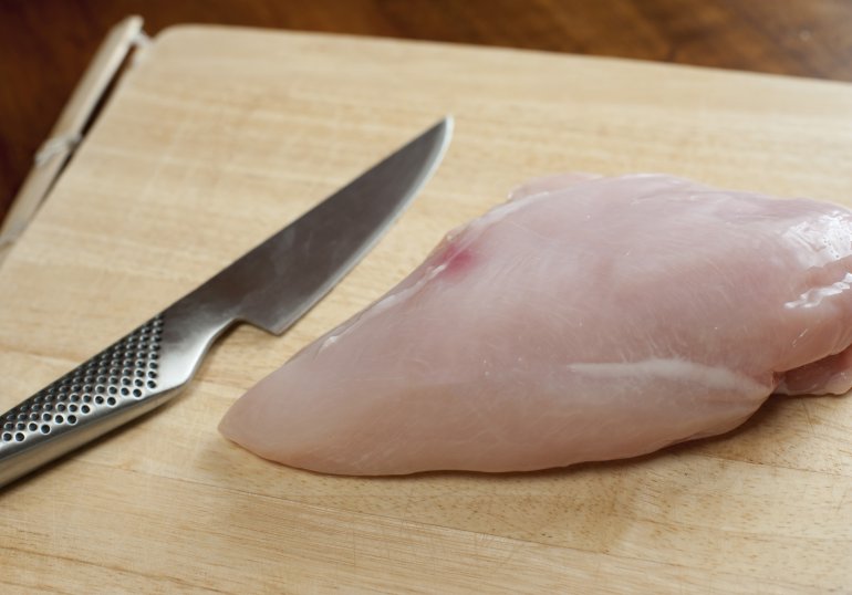 Uncooked lean healthy chicken breast on a wooden chopping board with a sharp kitchen knife , close up view