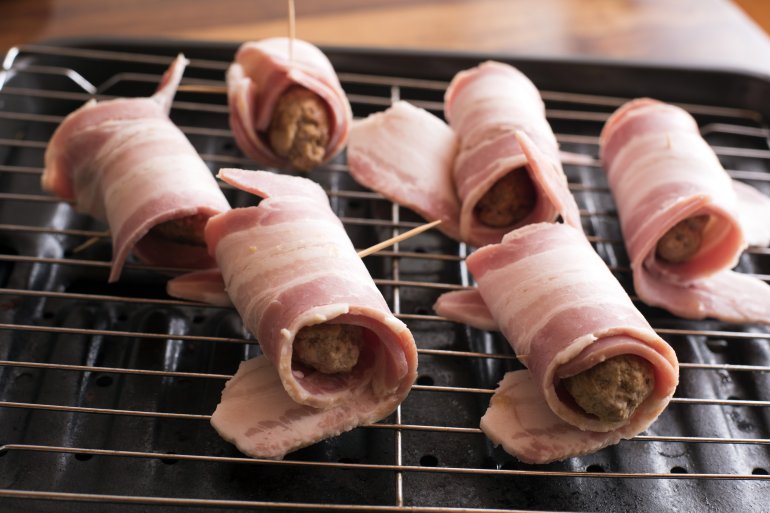 Uncooked bacon rolls or pigs in blankets with rashers of bacon around pork sausages ready on the grill for cooking