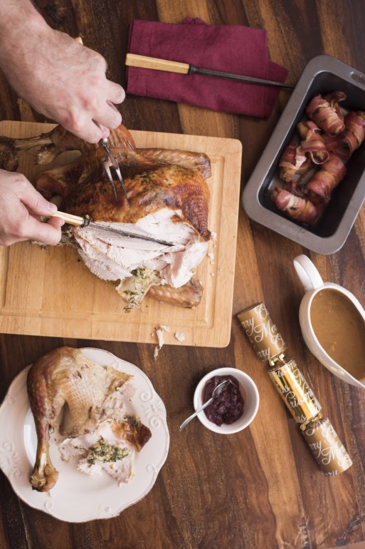 Man cutting thanksgiving turkey on wooden cutting board on a wooden table