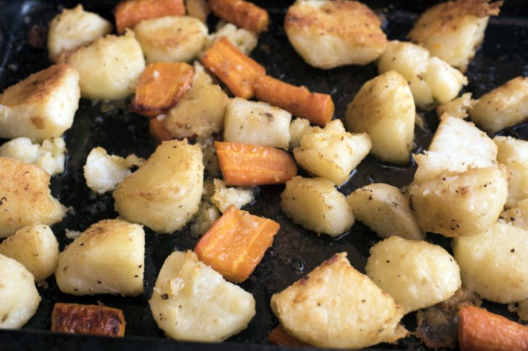 Oven roasted fresh potatoes and carrots in a baking tray waiting to be served as an accompaniment to dinner