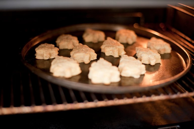Christmas cookies in the shape of Christmas trees baking in the oven on a round baking tray