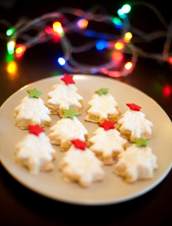 Festive Christmas cookies or biscuits n the shape of traditional Christmas trees decorated with little red and green stars with colourful party lights in the background