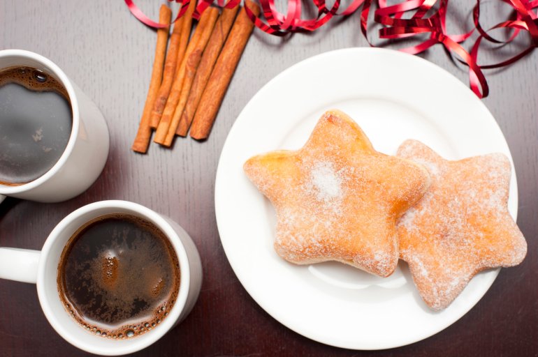 Overhead view of two mugs of freshly brewed coffee and festive Xmas doughnuts in the shape of a star served for refreshments