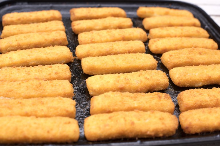 Full frame close up on freshly baked fish finger snacks on black oven tray for concept about breaded comfort food
