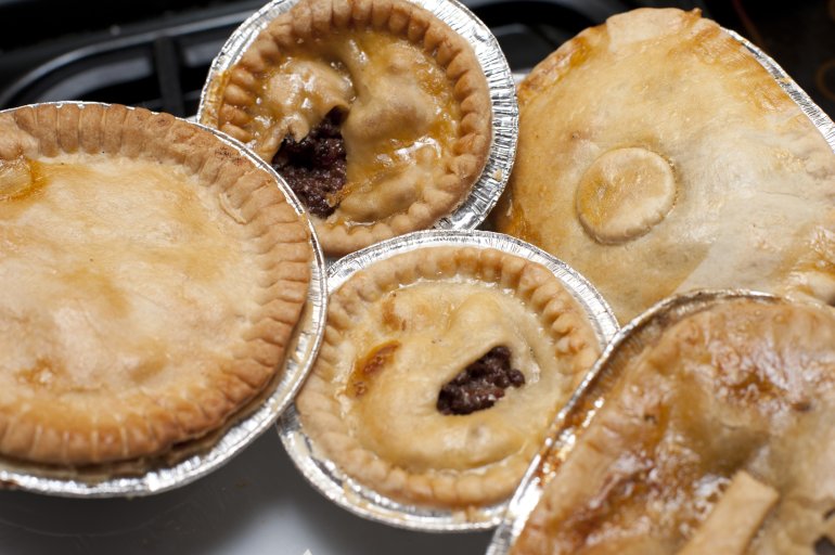Assortment of pastry meat pies in a bakery or store with different shaped crusts in disposable tin foil bases, close up overhead view