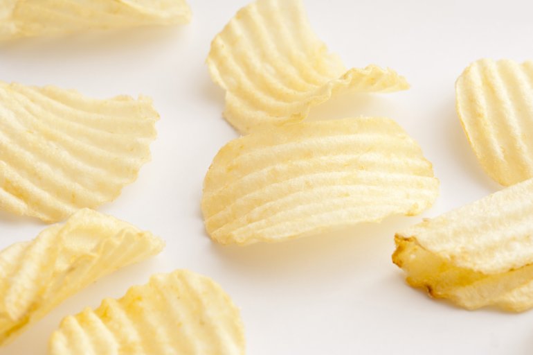 Close up view on various sized scattered ridged potato chips over white background surface