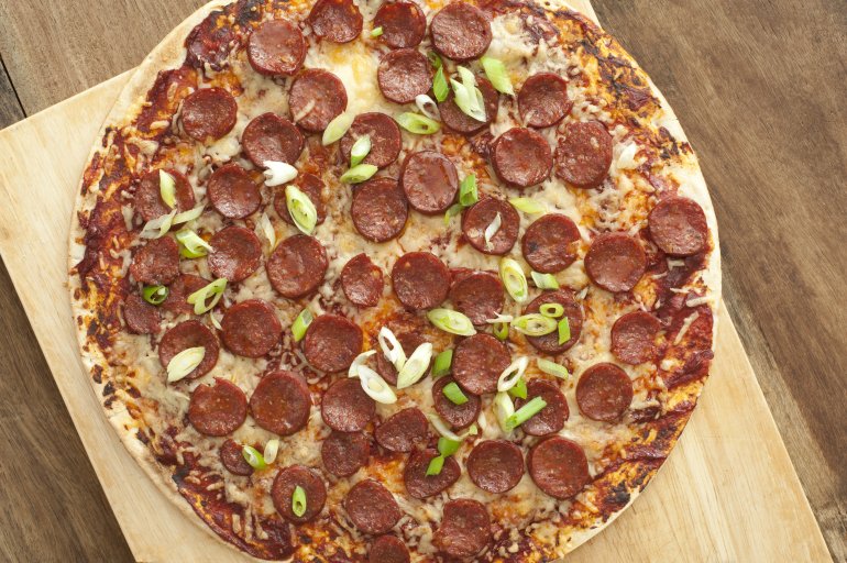 Whole pepperoni or salami pizza with mozzarella cheese and shallots on a crispy thin crust viewed from above on a wooden cutting board