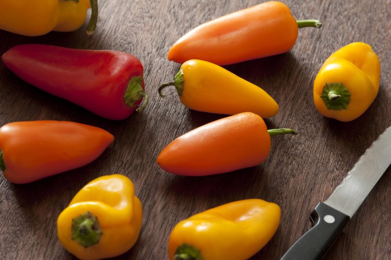 A close up of colourful, assorted capsicums on a wooden chopping block with knife.