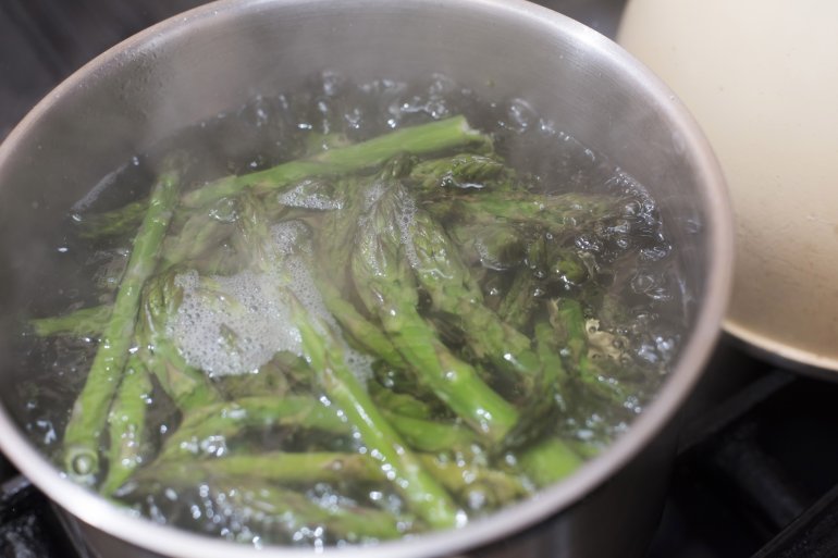 Fresh green asparagus spears being blanched in a pot of boiling water on a stove in a close up view