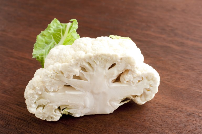 Sliced through head of fresh white cauliflower on a wooden chopping board viewed with focus to the cross-section