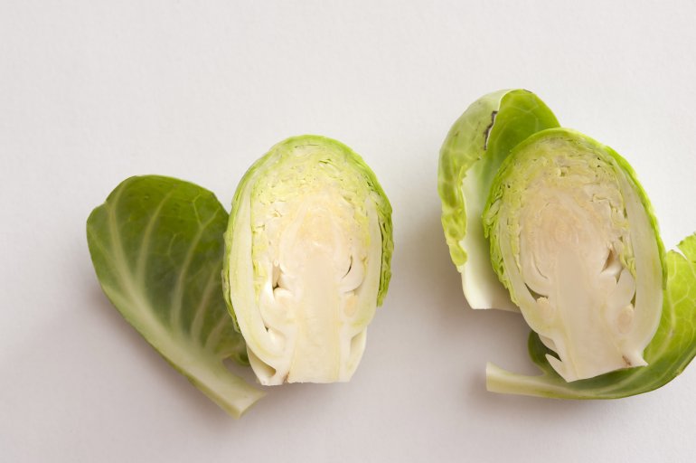 Fresh green Brussels sprout head cut in half, viewed in close-up on white surface background