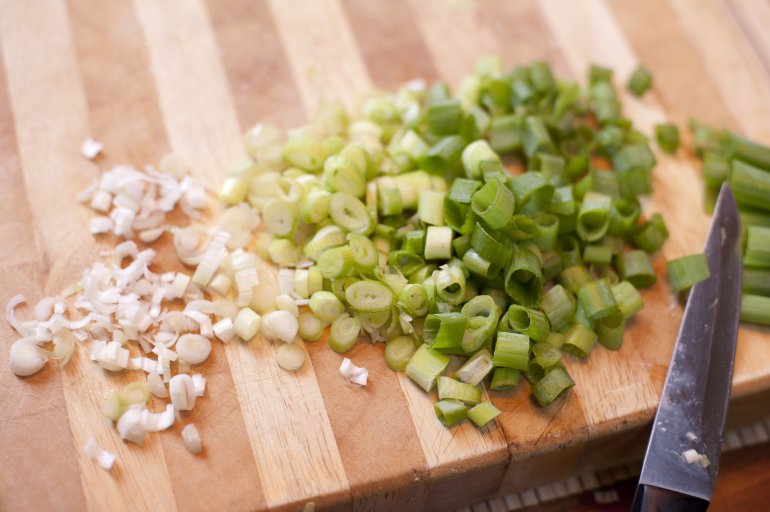 Chopped spring onion on wooden board with a knife